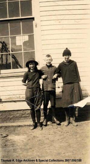 Portrait of two young girls and one boy in front of a wooden house or wooden store, [Alberta].