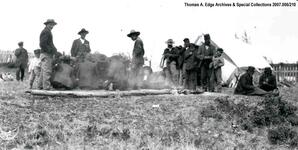 Indians standing by a tent while others are sitting beside an open fire, [Alberta].