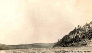 A river with trees on one shoreline, [Alberta]. Note on the back reads: Indian Treaty Party coming down the Laird River 1910"".