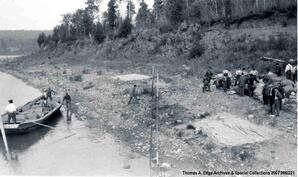 One scow landed on shoreline. There are supplies in scow and on shore and supplies are being unloaded from scow to shore, [Alberta].