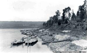 Numerous scows landed and four or more canoes on the shore. There are supplies in the boats and piles of supplies on the shore covered by cloths, [Alberta].