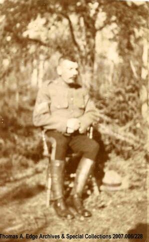 Portrait of a man in a military uniform, sitting on a chair in the woods, [Alberta]. Note on the back reads: ""Sargent Field just promoted May, 1909"".
