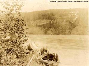 Two boats landed at a shore line. People and cloth coverings in both boats, [Alberta].