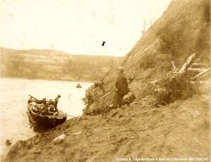 One boat landed on a steep shore. There are men in the boat and men standing on the shore, [Alberta].