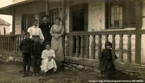A family outside a house in front of the porch, Fort Chippewyan.