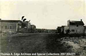 Dirt street in a town with wooden buildings on both side, Gibbons. Note on the back reads: ""Town of Gibbons, Alta., 1946.""