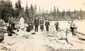 Portrait of ten people on a shore, one boy is holding onto a boat in a river, Sandy Bay