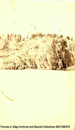 A body of water and across it is a very steep rocky shore, [Alberta].
