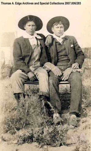 Portrait of two men sitting on a small bench in a field, [Alberta]. Note on the back reads: ""Local Metis, No. 1.""