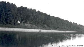 A shore line with one boat landed and one white tent in an area which is cleared, [Alberta].
