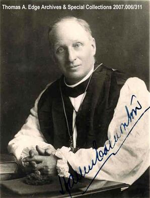 A portrait of one man sitting at a desk with his arms resting on the desk.