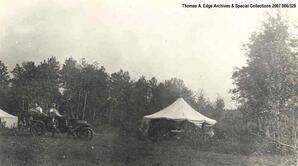 Six people in a car near two white tents, [Alberta].