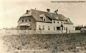 A large building with a flag on the roof, Hay River. Note on the front reads: "Hay River Mission".