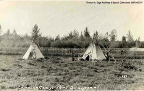 Two teepees in a field with a fence in the background, Fort Simpson. Note on the front reads: "Indian Camp - Fort Simpson".