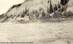A body of water and across it is a rocky shore, [Alberta]. Note on the back reads: "Athabasca River".