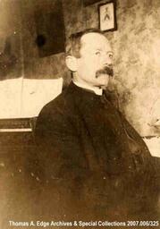 A portrait of a man taken inside a house, he is wearing a suit, [Alberta]. Note on the back reads: "Dad".
